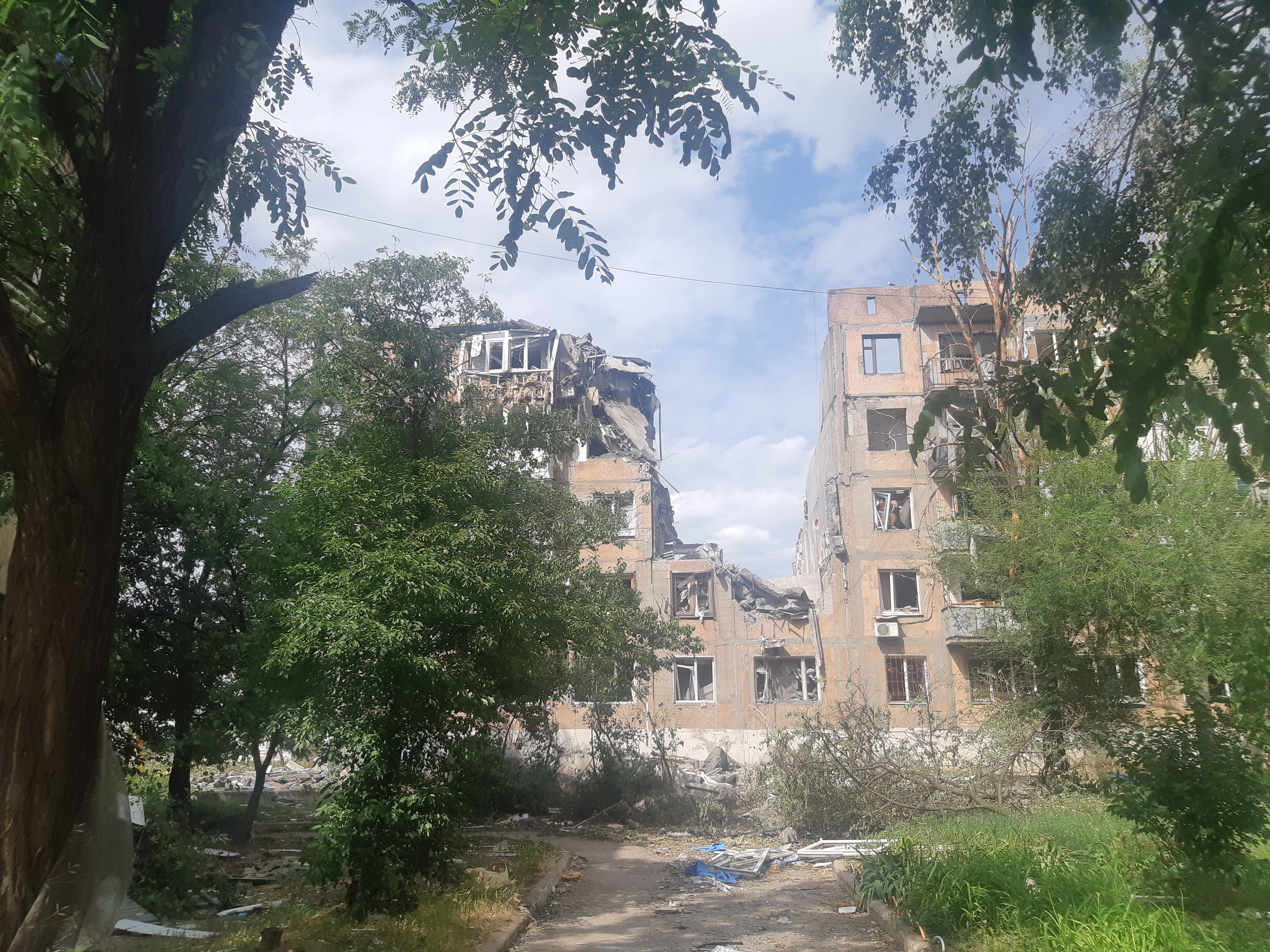 Destroyed multi-storey residential building in Ukraine seen through summer greenery